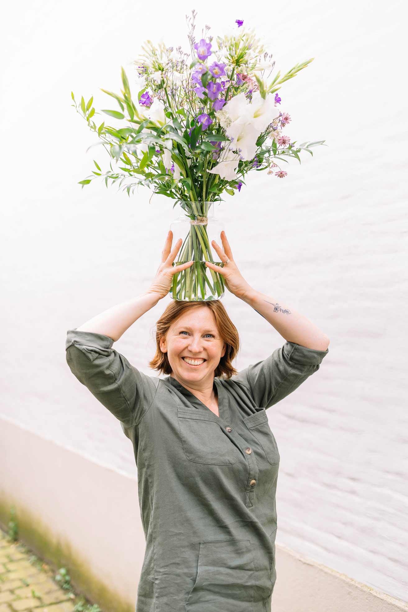 Kim houdt boven haar hoofd een vaas vast met een prachtig kleurrijk boeket verse snijbloemen