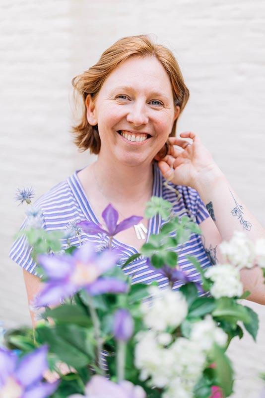 Kim van Fleurtop Kim lacht naar de camera op de voorgrond zie je een wazig boeket kleurrijke zijdebloemen